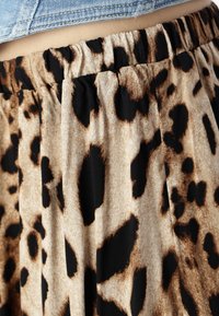 Hame leopardi-kuosisella, jossa on elastinen vyötärö. Taustalla on teksturoitu beige väri ja mustia sekä ruskeita laikkuja. Pleatattu muotoilu.
