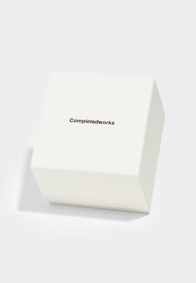 Λευκό τετράγωνο κουτί με ματ φινίρισμα. Έχει τυπωμένο το "Completedworks" σε μαύρη γραμματοσειρά στην κορυφή. Απλός και μίνιμαλ σχεδιασμός.