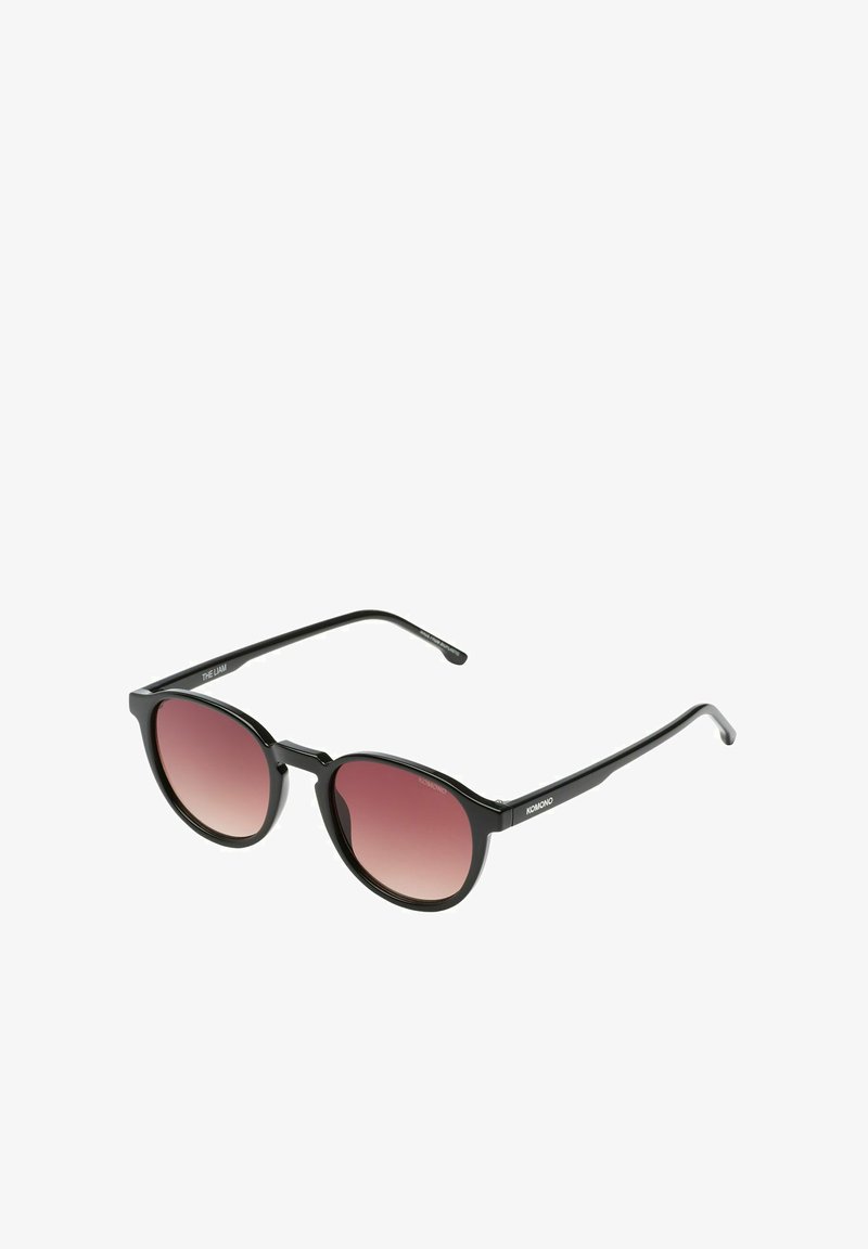 Lunettes de soleil rondes avec une monture noire brillante, des verres dégradés roses et des branches noires fines. Présente une inscription de la marque sur l'intérieur de la branche.