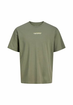 Teenager med krøllet hår iført olivengrøn "California" t-shirt, løse blå jeans og brune sko, der står mod en hvid baggrund.
