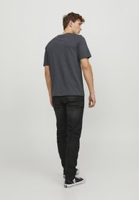 Mørkegrå kortærmet t-shirt lavet af bomuldsblandinger, kombineret med sorte jeans og sorte sneakers med hvide såler. Enkel, udekoreret design.