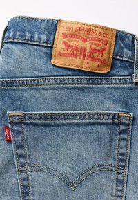 Niebieskie dżinsy z denimu z fakturowanym, wyblakłym wykończeniem, z brązową skórzaną metką z napisem "Levi Strauss & Co." oraz czerwoną logo na kieszeni.