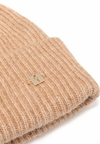 Beżowa dzianinowa czapka o prążkowanej fakturze, z złotą prostokątną metką. Miękki materiał i podwinięty brzeg podkreślają jej design.