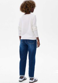 Pull en tricot blanc à manches longues, accompagné d'un jean en denim bleu. Le jean présente des ourlets retroussés et des poches arrière. Les chaussures sont des baskets noir et blanc.