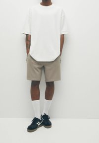 T-shirt blanche surdimensionnée, short beige et baskets noires avec accents blancs. Chaussettes blanches, texture lisse, coupe décontractée, design minimal.
