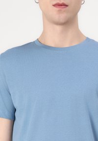 Ανοιχτό μπλε κοντομάνικη μπλούζα φτιαγμένη από μαλακό, λείο ύφασμα με στρογγυλή λαιμόκοψη. Διαθέτει έναν απλό σχεδιασμό χωρίς μοτίβα ή λεπτομέρειες.