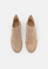 Beige mokkanahkasaappaat, joissa on sileä pinta ja joustavat sivupaneelit, pyöreä kärki ja tikatut yksityiskohdat pohjan ympärillä.