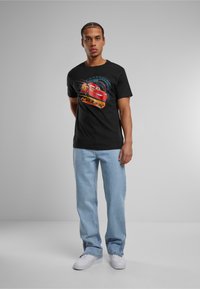 Sort bomulds T-shirt med et farverigt Lightning McQueen grafikdesign, parret med lyseblå denimjeans og hvide sneakers.