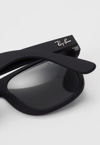 Svarte Ray-Ban solbriller med matt finish, runde linser og signaturlogo på stangen. Elegant design med buede kanter.