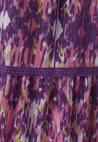 Tissu imprimé violet et rose avec des accents verts, doté d'une bande en crochet texturée à la taille et de plis verticaux sur toute la surface.