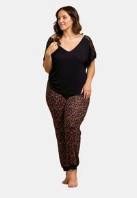 Haut noir à col en V avec des détails en dentelle, associé à un pantalon de jogging à motif floral coloré avec des poignets élastiques. Coupe décontractée et confortable pour un confort optimal.