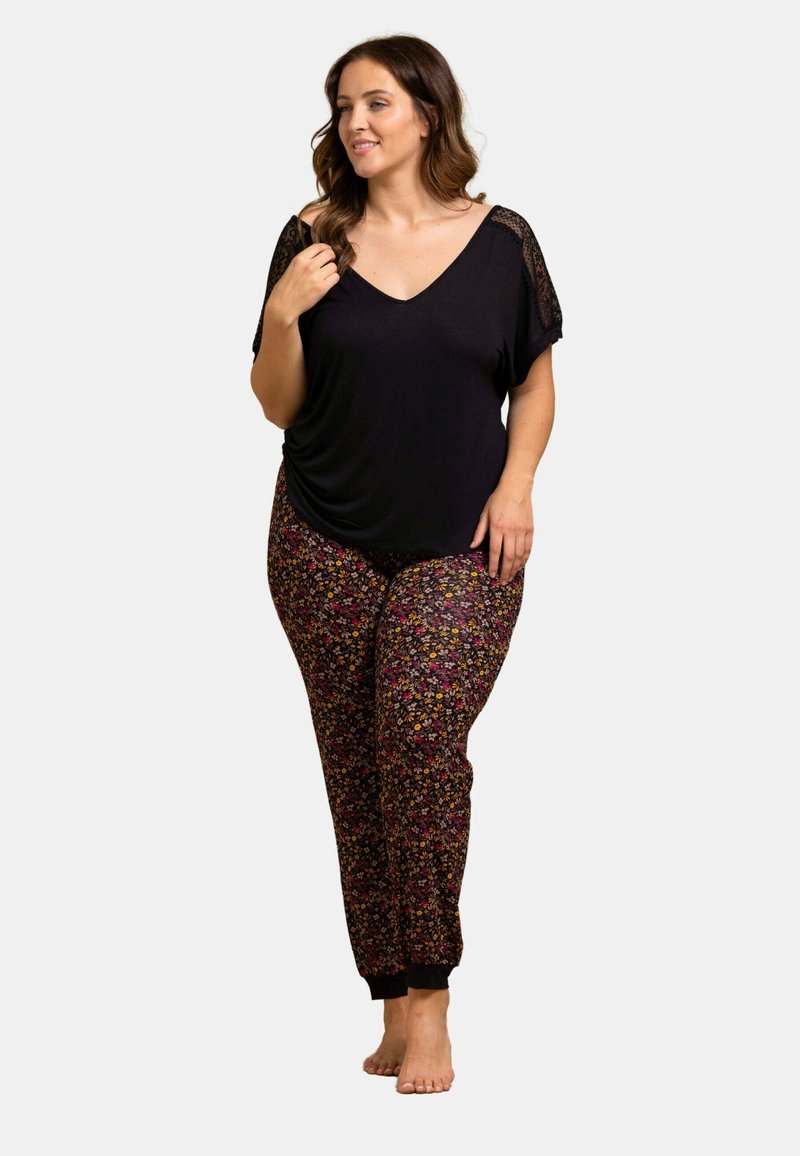 Haut noir à col en V avec des détails en dentelle, associé à un pantalon de jogging à motif floral coloré avec des poignets élastiques. Coupe décontractée et confortable pour un confort optimal.