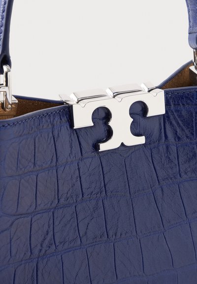 Τσάντα χειρός από μπλε δέρμα με υφή κροκό, με ασημένιο κούμπωμα και κοντό λουράκι, σε κοντινή λήψη του άνω μέρους και των λεπτομερειών της μεταλλικής κατασκευής.