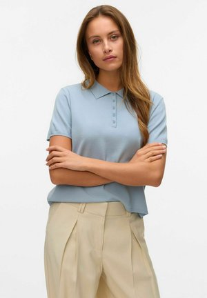 Camisa polo azul clara con cuello y tapeta de botones, hecha de una tela suave. Combinada con pantalones beiges a medida con pliegues.