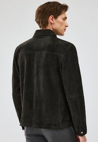 Giacca scura in suede con colletto e dettagli in bottone, caratterizzata da una superficie liscia e una forma su misura, mostrata da una vista posteriore.