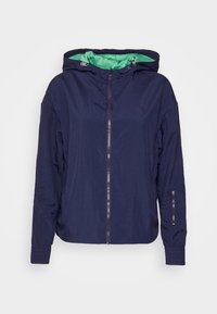 Námořnická lehká bunda s zelenou podšívkou, předním zipem a nastavitelnou kapucí. Obsahuje elastické manžety a zipovou boční kapsu.