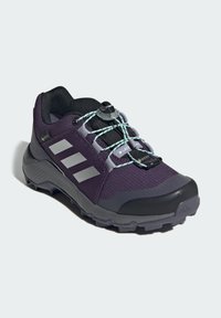 Chaussure de sport violette avec tige en mesh, semelle en caoutchouc grise, bandes réfléchissantes et système de laçage rapide pour un maintien sécuritaire.