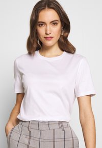 Weißes Kurzarm-T-Shirt mit rundem Ausschnitt. Weiches Baumwollmaterial zu grauen, karierten Maßanzughosen mit blauen und braunen Linien.