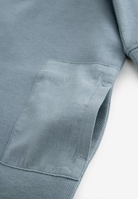 Tissu texturé bleu clair avec une grande poche plaquée lisse bleu clair cousue sur la surface.