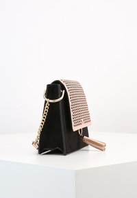 Svart mockaväska med en metallisk roséguldig perforerad flik, kedjerem och en tofsdetalj. Har en strukturerad form och en mjuk yta.