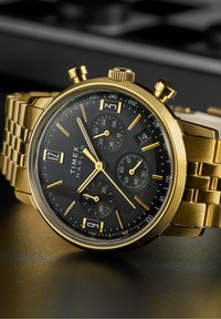 Montre chronographe dorée avec un cadran noir, accents argentés, affichage de la date et un bracelet en acier inoxydable à maillons.