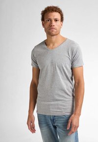 Tricou gri cu mânecă scurtă și decolteu în V, dintr-un material moale și ușor, asortat cu blugi albaștri deschiși. Tricoul are o croială slim și o textură fină.