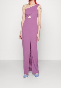 Asymmetrisk one-shoulder kjole i lilla jersey-stof med en frontslids og nøglerumsudskæring. Kombineret med lyseblå spidse hæle.