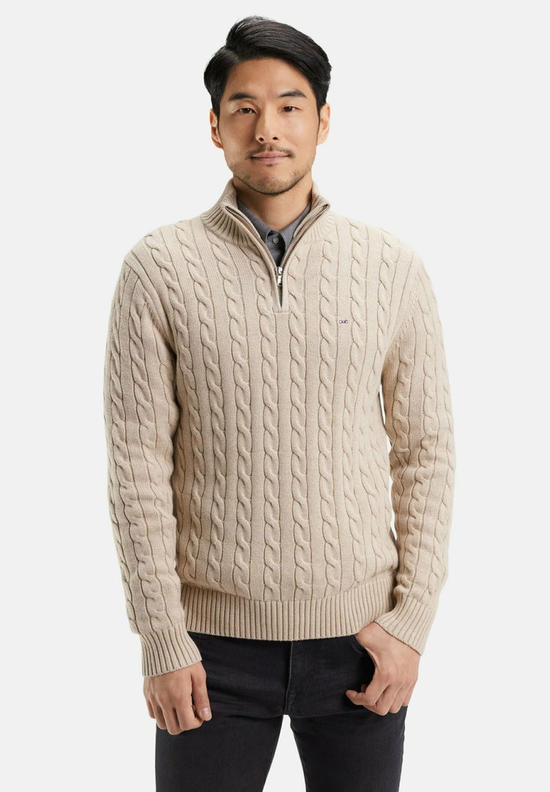 Pull en maille torsadée beige avec un col zippé, des poignets côtelés et un ourlet côtelé. Porté par-dessus une chemise sombre, présenté sur un mannequin masculin.