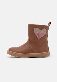 Bottines marron avec une finition en cuir texturé, arborant un patch en forme de cœur pailleté rose et une semelle en caoutchouc pour l'adhérence.