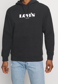 Sweat à capuche noir en tissu doux, avec une poche kangourou et le logo Levi's blanc sur la poitrine. Coupe décontractée avec des poignets côtelés.