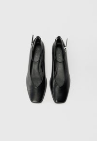 Scarpe in pelle nera con punta quadrata, lati aperti e una sottile cinturini alla caviglia con una fibbia in tonalità argento. Texture liscia e design minimalista.