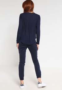 Marineblå langærmet bluse med plisseringer bagpå, parret med tapered marineblå joggers og hvide sneakers. Glat stof, afslappet pasform.