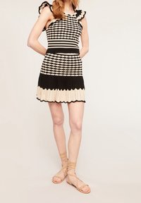 Abito lavorato a maglia nero e crema con motivo, spalline arricciate, corpetto aderente e gonna svasata. Abbinato a sandali beige con cinturini.