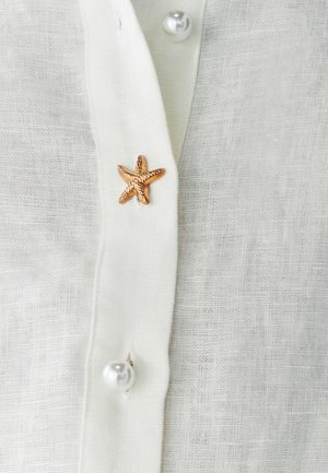 White linen shirt featuring a golden starfish accent and pearl buttons, with a textured fabric and simple collar design.