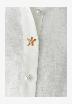 Balta lininė marška su auksine jūrų žvaigžde ir perlų sagomis, turinti tekstūruotą audinį ir paprastą apykaklės dizainą.