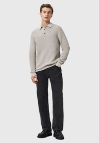Lichtgrijs gebreid poloshirt met een platte kraag, drie zwarte knopen, gedragen met zwarte denim broek en zwarte schoenen.