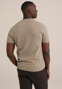 Krémový svetr s krátkým rukávem a texturovaným pleteným vzorem, s žebrovanými manžetami a lemem, nošený s tmavými kalhotami, pohled zezadu.