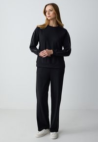 Black sweatshirt and sweatpants set, featuring long sleeves, a relaxed fit, and side accents. Made of soft fabric with subtle sheen.