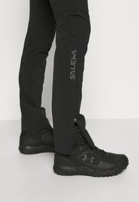 Voděodolné černé kalhoty s rozepínacími kotníky a reflexním logem "water". Kombinovány s černými vysokými sportovními botami.