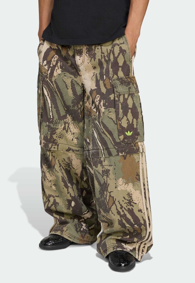 Pantalones cargo de camuflaje en tonos verdes y marrones, con grandes bolsillos laterales y una tela texturizada. Se llevan con zapatos negros.