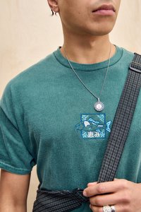 Green short-sleeve t-shirt featuring blue fish embroidery on chest, paired with a black checkered strap and silver chain necklace.