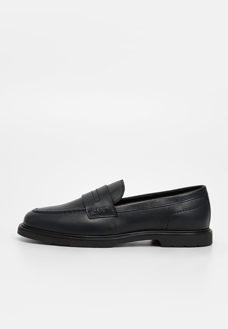 Mocassins en cuir noir avec une finition lisse, présentant une semelle plate et une sangle décorative à l'avant. Détails de couture subtils visibles.