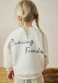 Off-white huppari, jossa on kirjailtu teksti "Tanssivat ystävät" tummansinisellä. Ominaisuuksiin kuuluu pyöreä kaula-aukko, ribbauskankaiset hihansuut ja rento istuvuus.