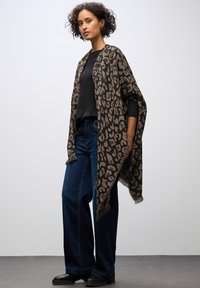 Djurmönstrad sjal i brunt och svart, med fransade kanter. Bärs över en svart topp, i kombination med mörkblå vida jeans och svarta stövlar.