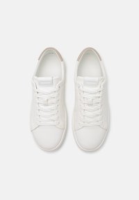 Baskets en cuir blanc avec bout arrondi, lacets plats et design minimaliste. Présente un tirant beige au talon et un logo en relief sur le côté.