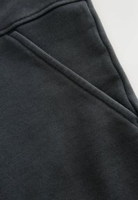 Tmavě šedá látka s texturovaným, žebrovaným povrchem; má diagonální detail švu probíhající napříč materiálem.