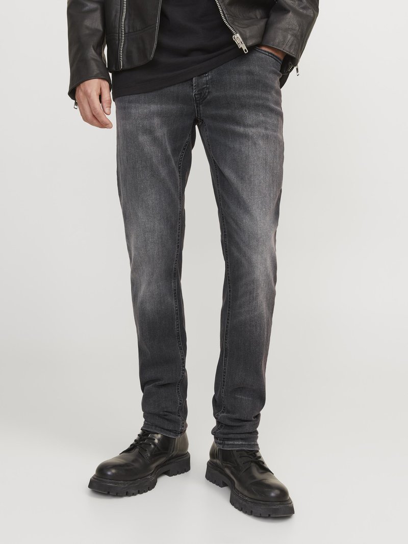 Graue Jeans aus Denim mit Slim Fit, die subtile Wisch- und Nahtdetails aufweisen, kombiniert mit schwarzen Schnürstiefeln und einer Lederjacke.