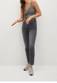 Top de tirantes gris acanalado combinado con jeans oscuros de talle alto, ligeramente desgastados. Modelo con zapatillas grises, de pie contra un fondo neutral.