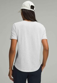 Hellgraues T-Shirt mit kurzen Ärmeln, abgerundetem Saum und glatter Textur. Kombiniert mit einer weißen Kappe mit verstellbarem Riemen.