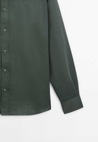 Donkergroene longsleeve shirt, gemaakt van gladde stof. Beschikt over een knoopsluiting aan de voorkant en een standaardmanchet met een lichte kromming aan de zoom.